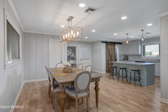 dining room with a barn door, a chandelier, light wood-type flooring, and ornamental molding