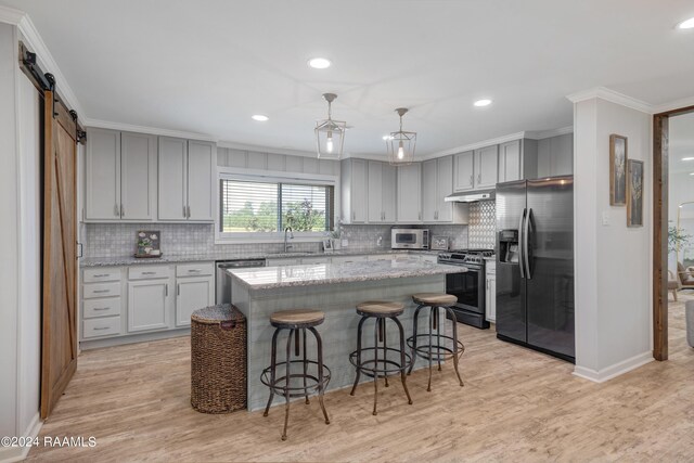 kitchen with ornamental molding, stainless steel appliances, pendant lighting, a barn door, and a center island