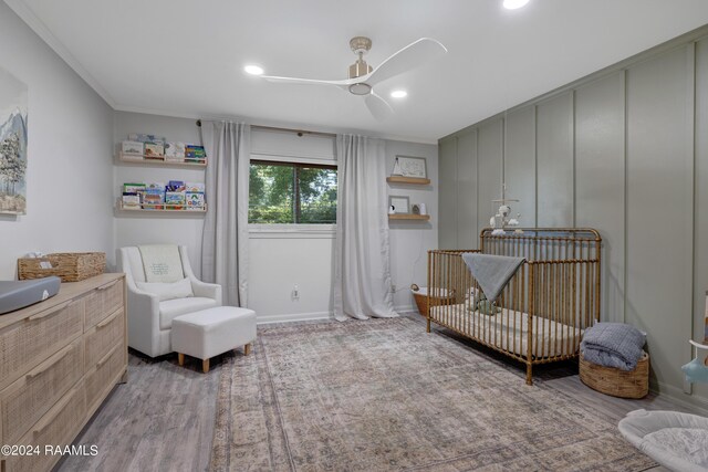 bedroom featuring light hardwood / wood-style floors, a nursery area, crown molding, and ceiling fan