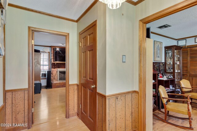 hallway with crown molding, a textured ceiling, and light hardwood / wood-style flooring