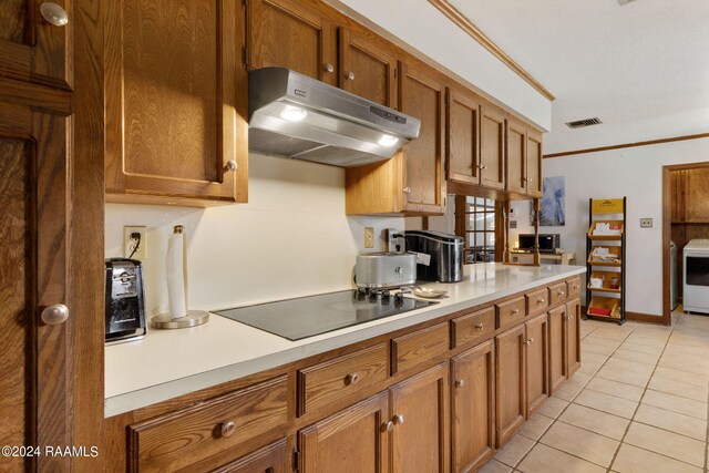 kitchen featuring a textured ceiling, light tile patterned floors, washer / dryer, ornamental molding, and black electric stovetop