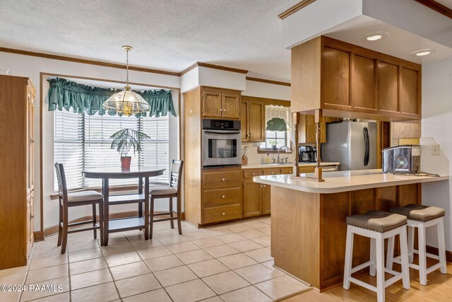 kitchen with a notable chandelier, ornamental molding, kitchen peninsula, sink, and appliances with stainless steel finishes