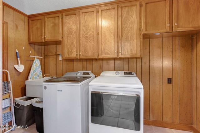 washroom featuring wood walls, light tile patterned floors, a textured ceiling, and separate washer and dryer