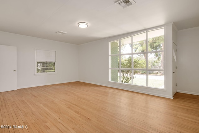 empty room featuring plenty of natural light, baseboards, visible vents, and light wood finished floors