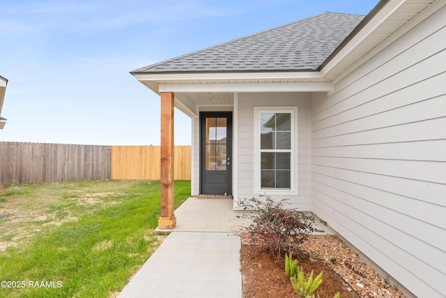 entrance to property featuring a yard, roof with shingles, and fence