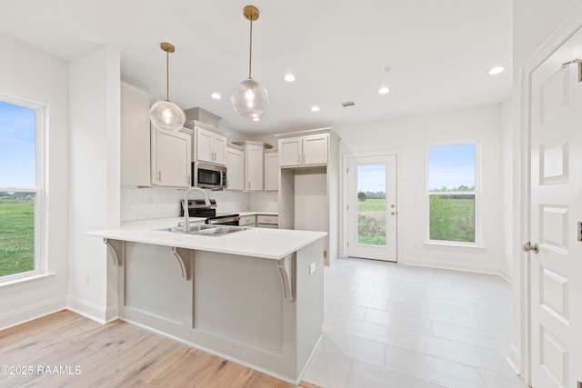 kitchen featuring a peninsula, appliances with stainless steel finishes, light countertops, a sink, and decorative backsplash