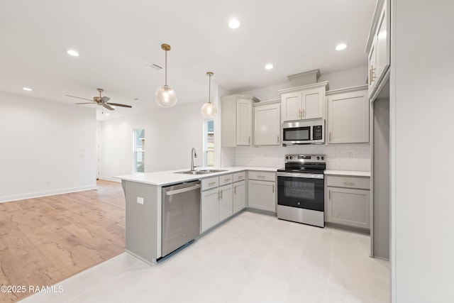 kitchen featuring tasteful backsplash, a peninsula, gray cabinetry, stainless steel appliances, and a sink