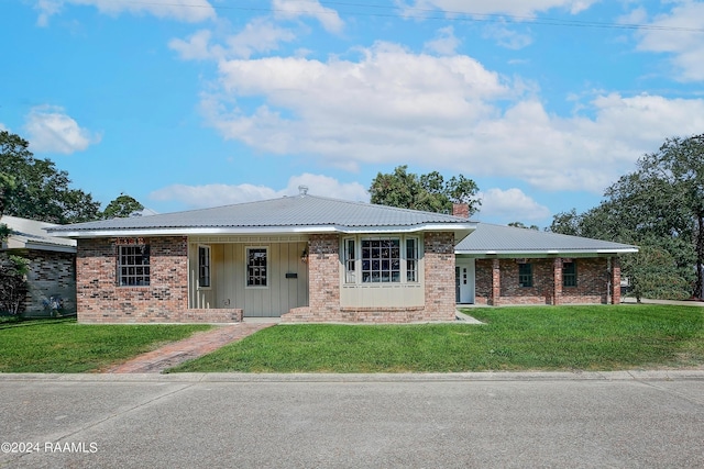 ranch-style house with metal roof, a chimney, a front lawn, and brick siding