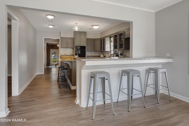 kitchen featuring glass insert cabinets, a kitchen breakfast bar, gray cabinetry, light wood-type flooring, and black oven