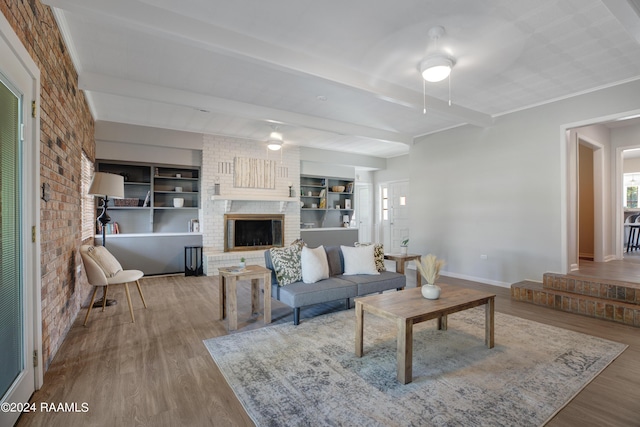 living room with a fireplace, brick wall, wood finished floors, beamed ceiling, and baseboards