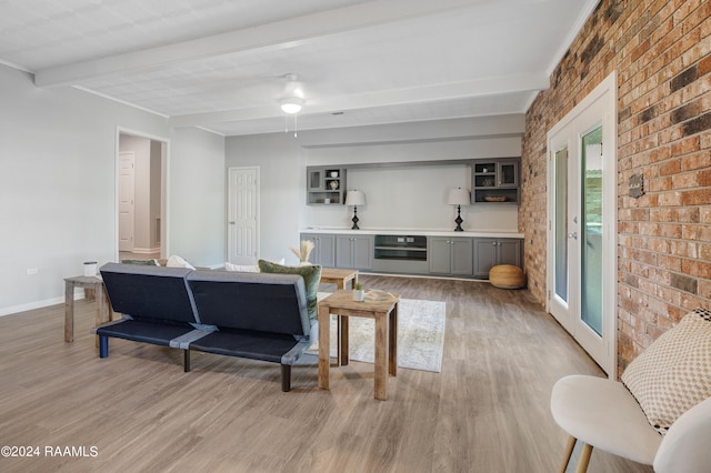 living area featuring light wood-type flooring, brick wall, baseboards, and beamed ceiling