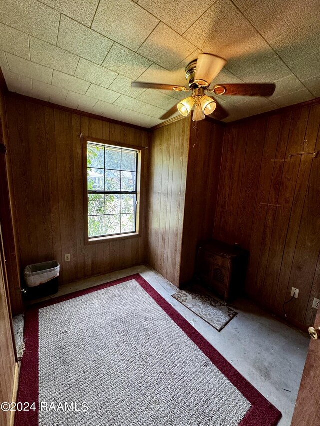 empty room with ceiling fan, wood walls, and a wood stove