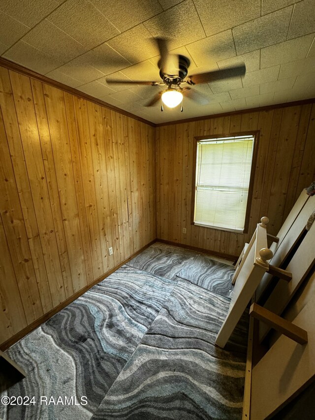 bedroom with ceiling fan, carpet floors, wooden walls, and ornamental molding