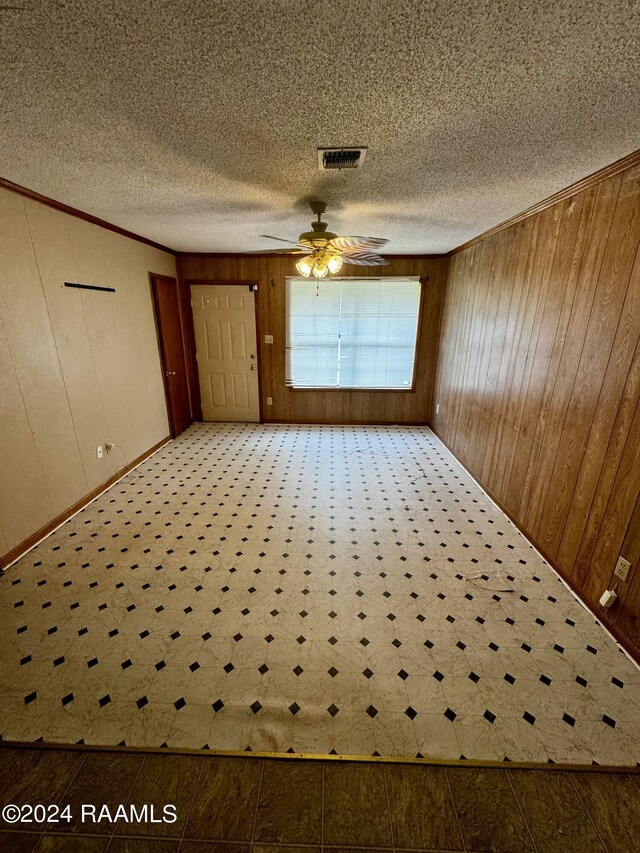 unfurnished room with a textured ceiling, ceiling fan, wooden walls, and crown molding