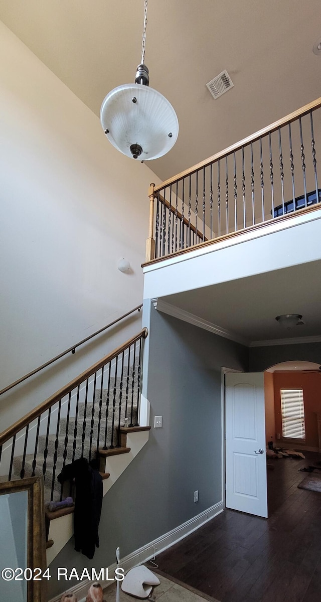 staircase featuring crown molding, wood-type flooring, and a high ceiling