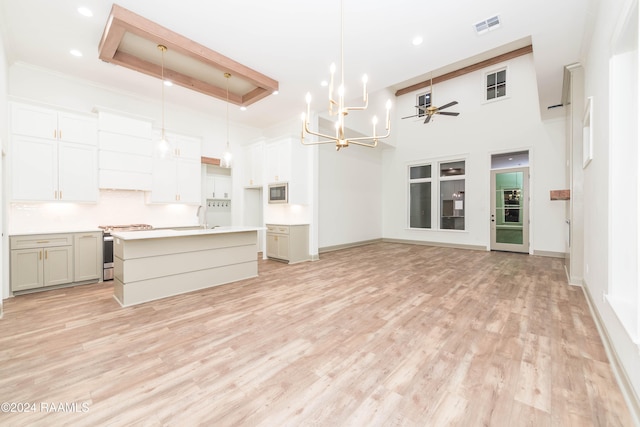 unfurnished living room with a raised ceiling, a high ceiling, ceiling fan with notable chandelier, and light wood-type flooring