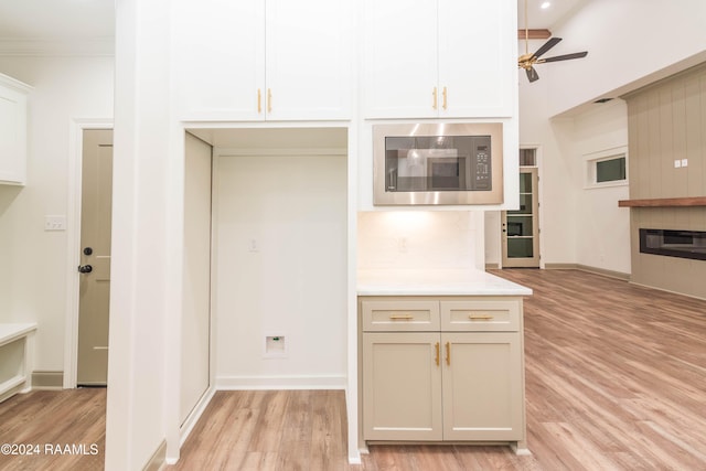 kitchen featuring built in microwave, ceiling fan, ornamental molding, a tiled fireplace, and light wood-type flooring