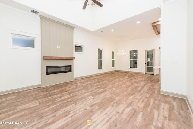 unfurnished living room featuring ceiling fan with notable chandelier, a large fireplace, and light hardwood / wood-style flooring