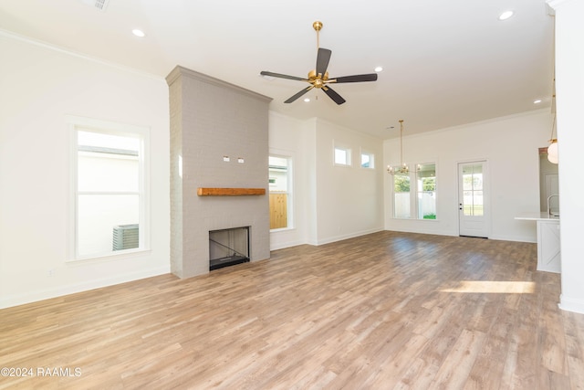 unfurnished living room with ceiling fan with notable chandelier, light wood-type flooring, ornamental molding, and a brick fireplace