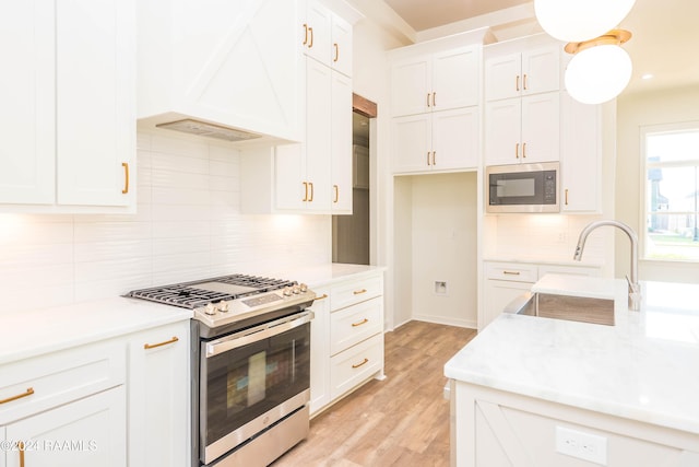 kitchen with premium range hood, sink, built in microwave, gas stove, and white cabinetry