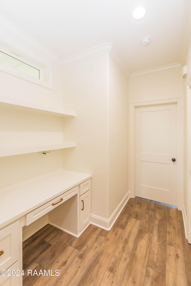 interior space with crown molding, built in desk, and light wood-type flooring