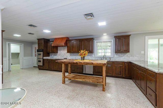 kitchen with custom exhaust hood, tasteful backsplash, visible vents, double oven, and a sink