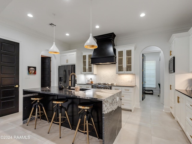 kitchen with arched walkways, backsplash, a sink, premium range hood, and black appliances