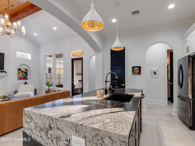 kitchen featuring arched walkways, a sink, visible vents, freestanding refrigerator, and a center island with sink