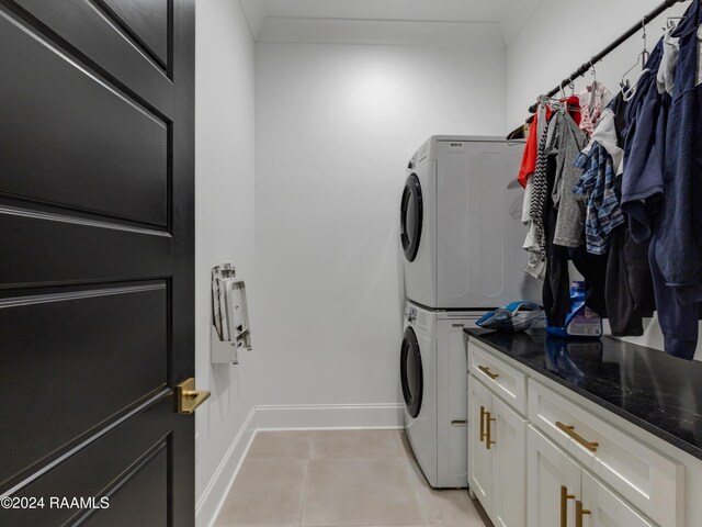 laundry room with light tile patterned flooring, stacked washer / dryer, and cabinets