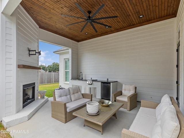 view of patio featuring ceiling fan, a sink, fence, exterior kitchen, and an outdoor living space with a fireplace