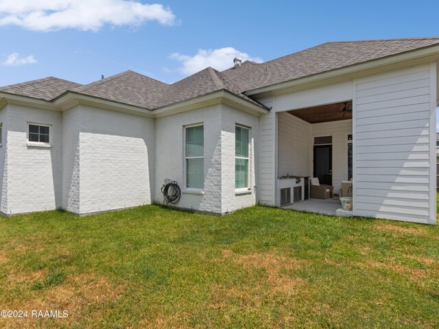 rear view of property with ceiling fan, a patio, and a lawn