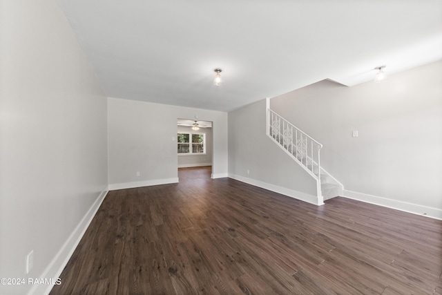 unfurnished living room featuring stairway, dark wood-type flooring, and baseboards