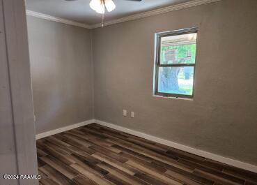 unfurnished room with ceiling fan, crown molding, and dark wood-type flooring