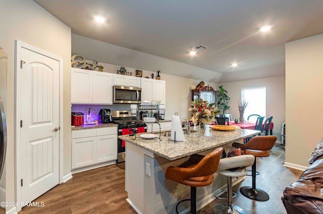 kitchen with white cabinets, wood-type flooring, a kitchen island with sink, and stainless steel appliances