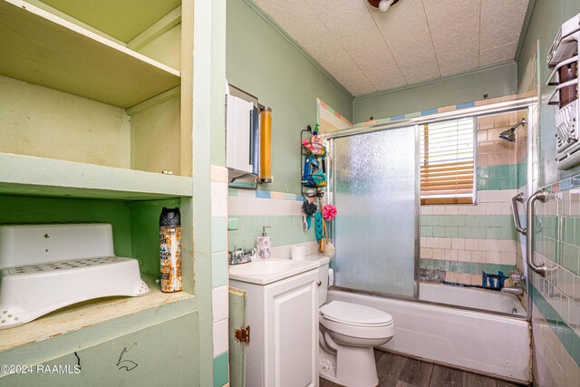 full bathroom with toilet, vanity, wood-type flooring, enclosed tub / shower combo, and tile walls