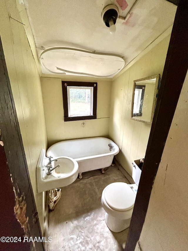 full bathroom featuring toilet, wood walls, a sink, and a freestanding bath
