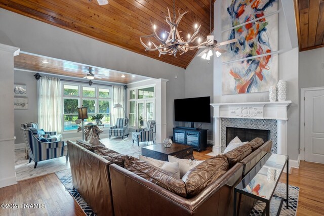 living room featuring light wood-type flooring, ceiling fan with notable chandelier, a tiled fireplace, and wooden ceiling