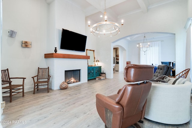 living room featuring beamed ceiling, a towering ceiling, a notable chandelier, and light hardwood / wood-style flooring