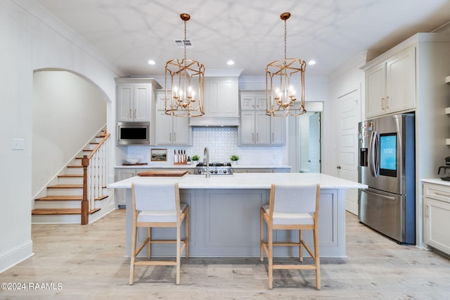 kitchen with backsplash, stainless steel appliances, light hardwood / wood-style floors, and a center island with sink