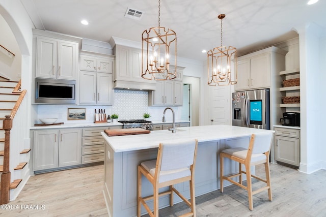 kitchen featuring light wood-type flooring, pendant lighting, tasteful backsplash, a kitchen island with sink, and stainless steel appliances