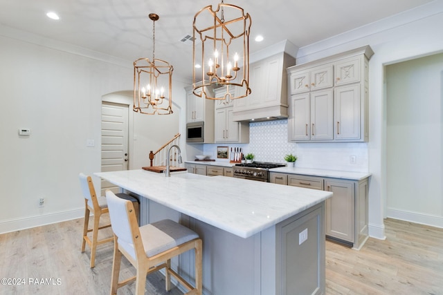 kitchen with light hardwood / wood-style flooring, tasteful backsplash, custom exhaust hood, range, and decorative light fixtures