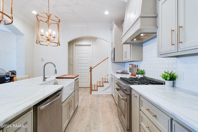 kitchen with decorative backsplash, light hardwood / wood-style flooring, premium range hood, light stone counters, and stainless steel appliances