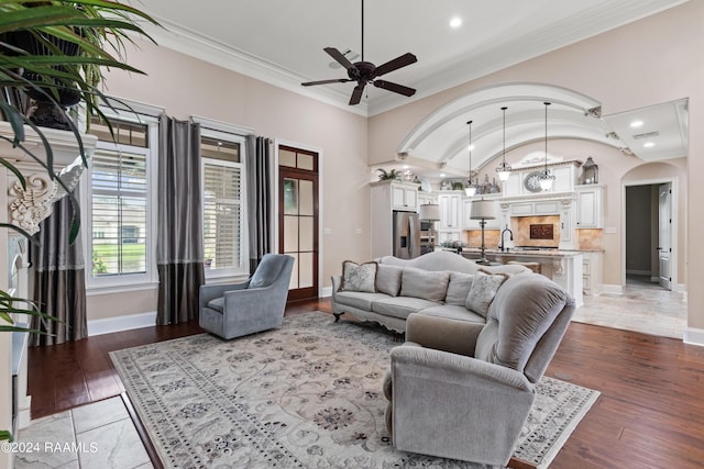 living room featuring arched walkways, lofted ceiling, wood finished floors, baseboards, and ornamental molding