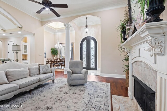 living room with ceiling fan with notable chandelier, hardwood / wood-style flooring, crown molding, and decorative columns