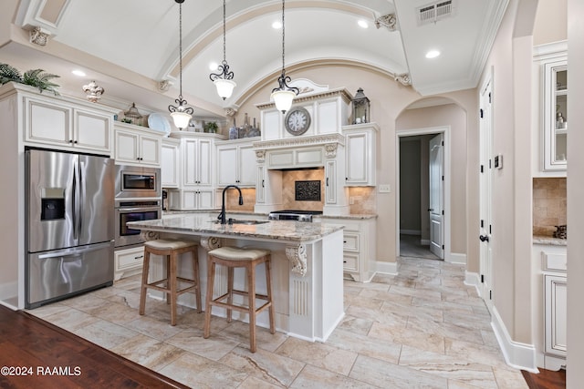 kitchen featuring backsplash, sink, appliances with stainless steel finishes, light stone counters, and an island with sink