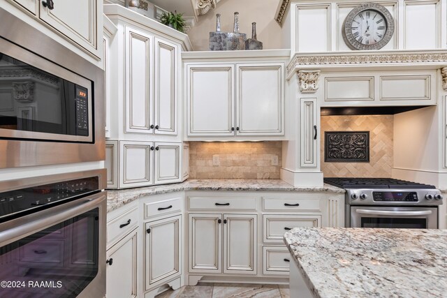 kitchen with appliances with stainless steel finishes, light stone counters, light tile patterned floors, and backsplash