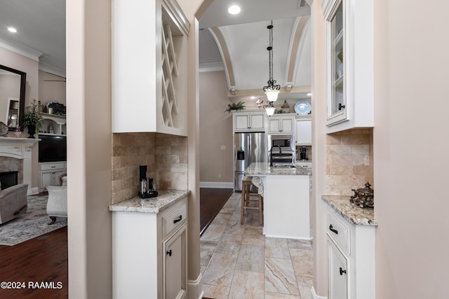 kitchen with light stone counters, glass insert cabinets, a kitchen breakfast bar, stainless steel appliances, and pendant lighting