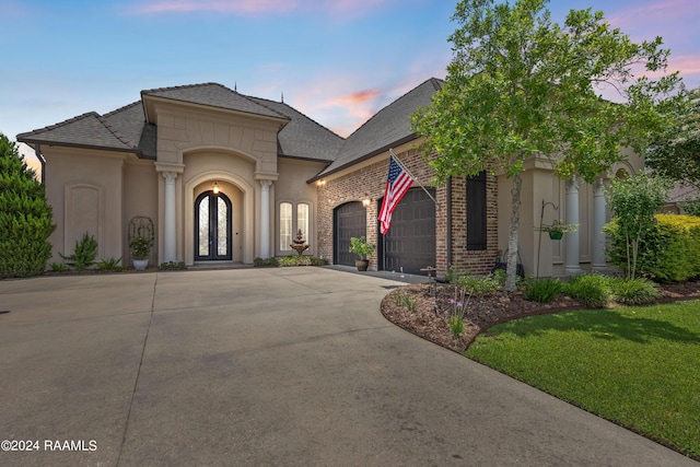 french provincial home with driveway, brick siding, an attached garage, and stucco siding