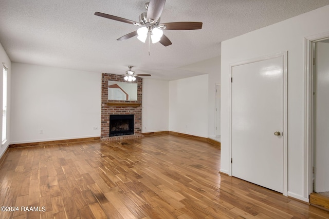 unfurnished living room with light wood-type flooring, ceiling fan, a textured ceiling, and a brick fireplace