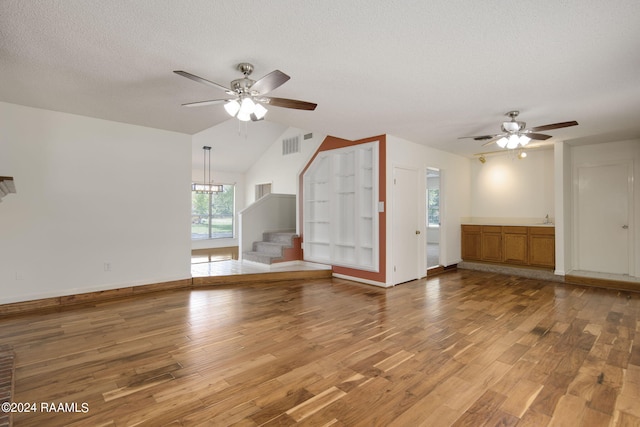 unfurnished living room with a textured ceiling, ceiling fan, hardwood / wood-style floors, and vaulted ceiling